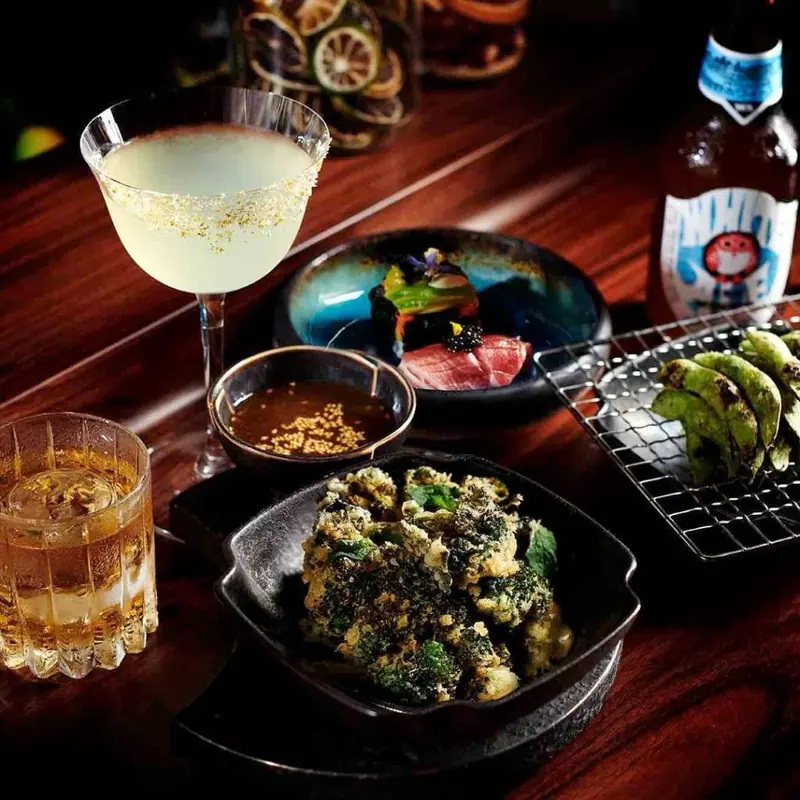 A cocktail, a Japanese whisky and small plates on a rosewood table